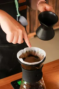 Hand pours hot coffee into a paper filter over a carafe while brewing at a specialty coffee workshop in Lijiang