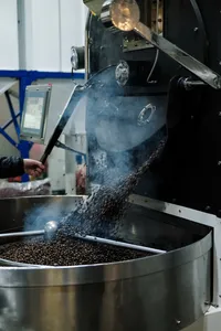 Coffee beans tumbling in a stainless roaster in Hoi An’s early-morning workshop, with steam rising from the machine