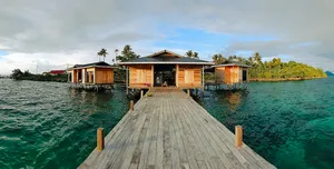 Wooden stilt sea lodges on a tropical island coastline, with a walkway leading out over clear water in Semporna