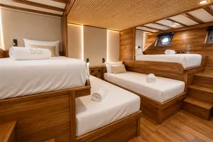 Travass Life shared cabin on a new phinisi with three neatly made single beds, wooden finishes and soft lighting for Komodo Island