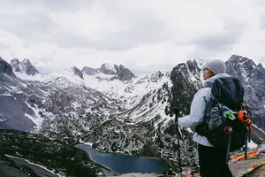 Trekker in a beanie with a large backpack gazing over snow-dusted mountain valleys and a turquoise lake in Shangri-La