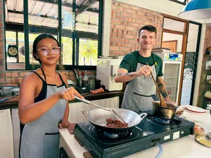 Cooking Malaysian comfort food with two people stirring a wok on a stovetop inside Kebun Lidstari’s farmhouse kitchen, Langkawi