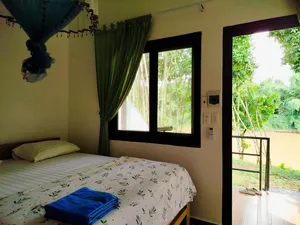 Green Hope Lodge bedroom corner with patterned duvet and green curtains, looking out from the terrace to rainforest greenery at Cat Tien