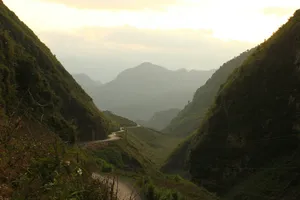 Misty mountain valley at sunrise with a winding track through green hills and distant ridges in China