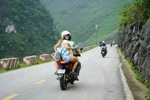 Helmed rider on a motorbike following a mountain road with other bikes across Ha Giang, on Mama’s Ha Giang loop