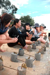 Travellers kneeling in shallow water filling coral planting frames with cement during the Rinca Coral Nursery Program on Komodo Island