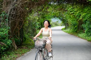 Cyclist riding along a quiet road enveloped by tropical greenery in Cat Ba, with a front basket and relaxed posture