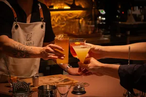 Beberapa tangan mengangkat dua koktail per gelas dengan hiasan jeruk untuk bersulang di bar koktail intim di Singapura.