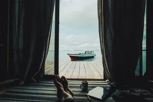 Curtains open inside a sea-lodge cabin at Semporna, looking out at a boat moored beside the wooden pier