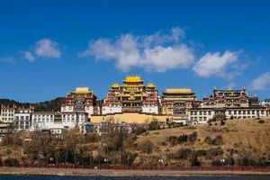 Shangri-La hillside temple complex with layered golden roofs and ornate red-and-white ramparts under a clear blue sky