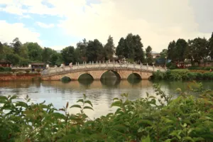 Stone arched bridge spanning a canal with lush trees in Lijiang Old Town during a local-guided Hidden Stories walk