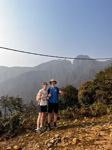 Two hikers pause on a mountain trail above Sapa as ridgelines rise behind them, towards Mt Fansipan