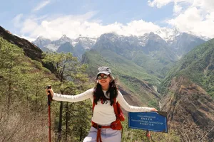 Backpack hiker smiling by a trail sign at a mountain lookout over Tiger Leaping Gorge in Lijiang during the 2D1N high trail