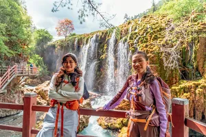 Two travellers pose at a wooden railing by a multi-tier waterfall near Shangri-La during a 6-day trek loop