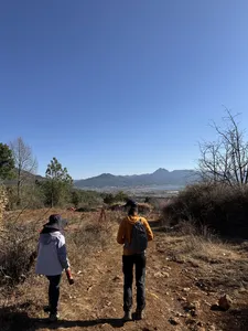 Backpackers hike a country trail in Lijiang toward a wide mountain valley, with Xintuo Ecotourism on the Yi & Naxi trek