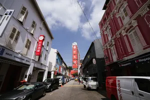 Singapore Chinatown street with shopfronts, parked cars and red heritage buildings, as a team explores alleys to find Singapore hidden gems