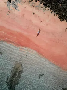 Aerial view of a swimmer in shallow pinkish water near the shoreline and rocks during a 3D2N shared Komodo cruise — Komodo Island