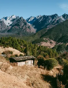 Rugged village hut overlooking pine valley and snowcapped peaks on the way to Wenhai Wetlands from Lijiang