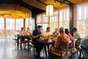 People enjoy a shared lunch at a long wooden table with Vietnamese dishes in a bright Hanoi restaurant for the agarwood tour