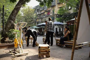 Community gathering in a shaded courtyard in Hanoi, with people relaxing near outdoor seats and swings under trees.