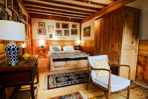 Wood-panelled guest room at Ferme Liotard in Shangri-La, featuring a carved bed, armchairs and patterned rugs for the stay