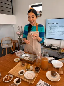 The TCM Chef smiling while holding a small glass of layered mocktail, with a learning screen behind, in workshops in Singapore
