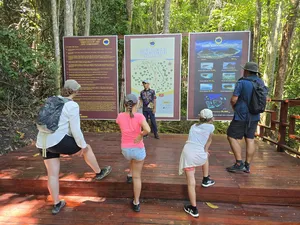 Bigfin Divers hike briefing in Semporna: travellers walk a wooden boardwalk beside marine maps in the forest
