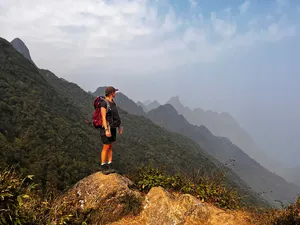 Single trekker pauses on a rocky viewpoint over the Fansipan range near Sapa during an eco day hike in mountain haze