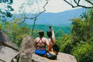 Backpackers seated on a boulder overlooking a lush valley in Hoi An, pausing for views during a waterfall motorbike adventure