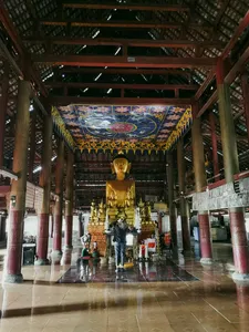 Patung Buddha emas di dalam aula kuil di Xishuangbanna dalam perjalanan sehari pribadi bersama pemandu lokal, interior dengan pilar merah