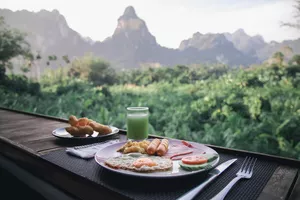 Outdoor breakfast set on a wooden table at Anurak Lodge—eggs, toast and fruit—during a stay in Khao Sok National Park