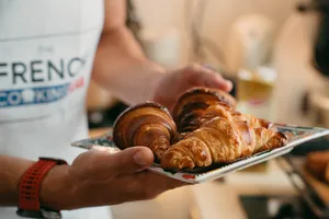 French chef in a French Cooking Lab apron presenting freshly baked golden croissants on a tray in Singapore
