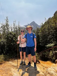 Two hikers pause on a narrow trail through tall grass near Mt Fansipan in Sapa, trekking with poles on a 1-day eco trek