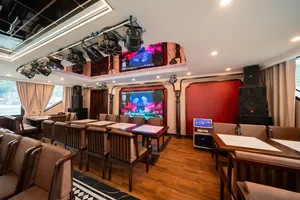 Dining and lounge area on a luxe Cat Ba cruise, with set tables, lounge seating, and a large TV entertainment screen
