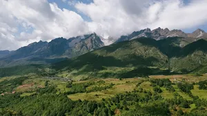 Lush green landscape around steep peaks near Lijiang, viewed from above with scattered clouds drifting over the mountains