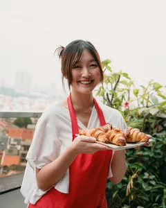 Smiling participant holding a tray of croissants on a balcony with city views, during a French Cooking Lab class in Singapore