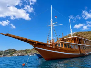 Newest wooden phinisi with raised masts and Indonesian flag cruising across blue water off Labuan Bajo