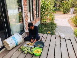 Kebun Lidstari host preparing food on a wooden porch in Langkawi, with fresh coconuts, pots and a white dog