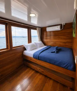 Wooden phinisi cabin with a double bed and sea view windows on a shared Komodo cruise, sailing from Labuan Bajo