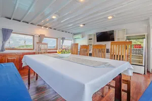 Boat dining room with pressed tables and windows, set for guests during a 3-day join-in Komodo boat trip in Labuan Bajo