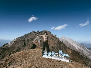 Hiker posing by a stone sign reading Jade Dragon 1st Peak, 4250m, during a guided summit hike in Lijiang