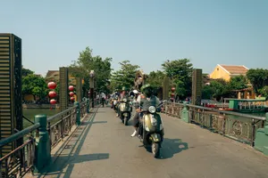 Deretan skuter Vespa melaju di sepanjang dermaga tepi sungai di Hoi An bersama Hoi An Backroad Tours, menuju serunya naik perahu keranjang