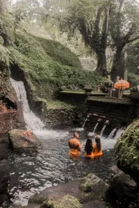 People relaxing in a natural rock pool with a waterfall in Indonesia during a yoga retreat, seated and soaking in warm water