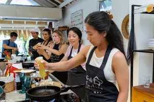 Gili T cooking class in Lombok: group members pour and stir ingredients at a shared stovetop station, led by locals