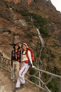 Two hikers with backpacks pause by a barrier overlooking a waterfall in Tiger Leaping Gorge near Lijiang on the 2D1N high trail