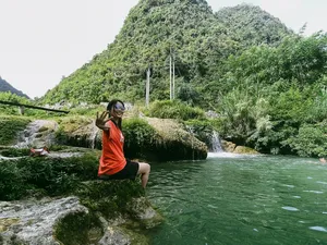 Traveller relaxing on a river rock by a waterfall in Cao Bang, Vietnam, amid lush green jungle on a motorbike loop