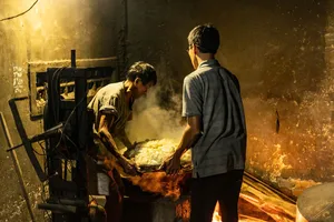 Blacksmiths working by a blazing forge in Hoi An, one man holding hot metal while another turns tools near the fire