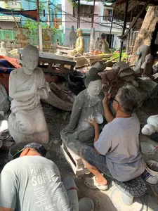 Saigon sculpture workshop where artisans work on white clay statues, with plaster figures and tools arranged along a sunlit aisle