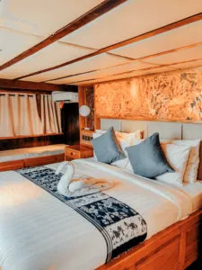 Luxurious cabin with made-up double bed and blue cushions on a Deluxe phinisi, ready for restful nights on a Komodo cruise, Labuan Bajo