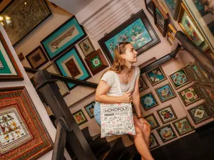 Woman carrying a HIDDEN Singapore Monopoly tote and looking up at colourful framed walls during the game in Singapore hidden gems